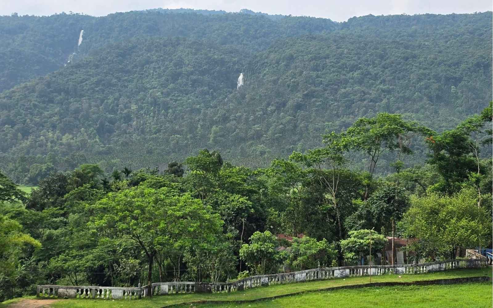 Forested hills with waterfalls streaking the far slope, seen over a balustraded ground