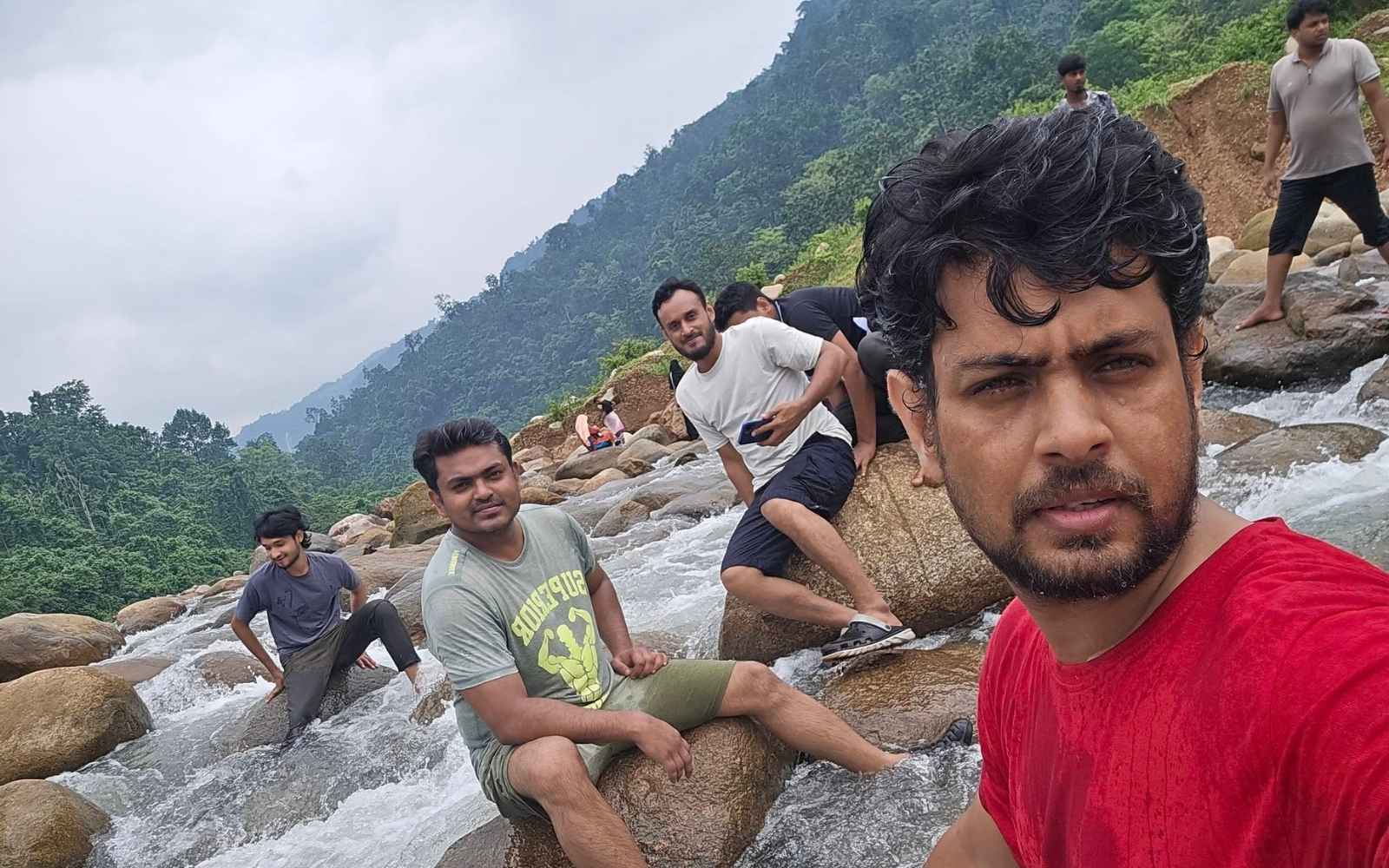 Team members sitting on boulders in a rushing stream, hills behind